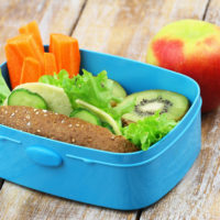 Healthy school lunch consisting of brown cheese roll, fresh carrots and kiwi fruit and apple