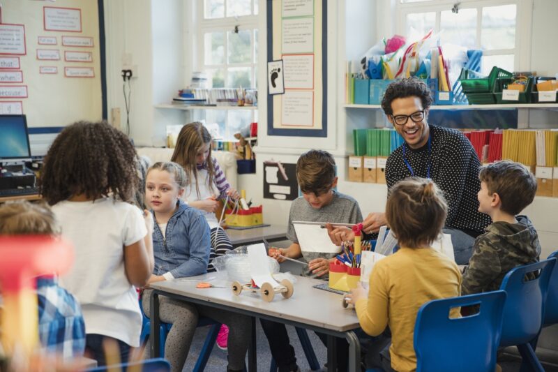 Elementary school children build 3d models using recycled materials with their teacher during class.