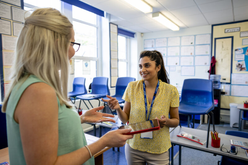 An over-the-shoulder view of two female teachers having a pre-school meeting and sharing teaching ideas with each other.