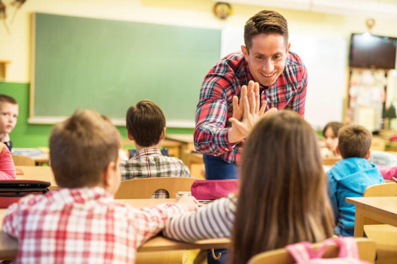 Happy elementary teacher congratulating his student