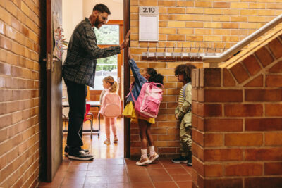 Elementary school teacher greeting his students at the door.