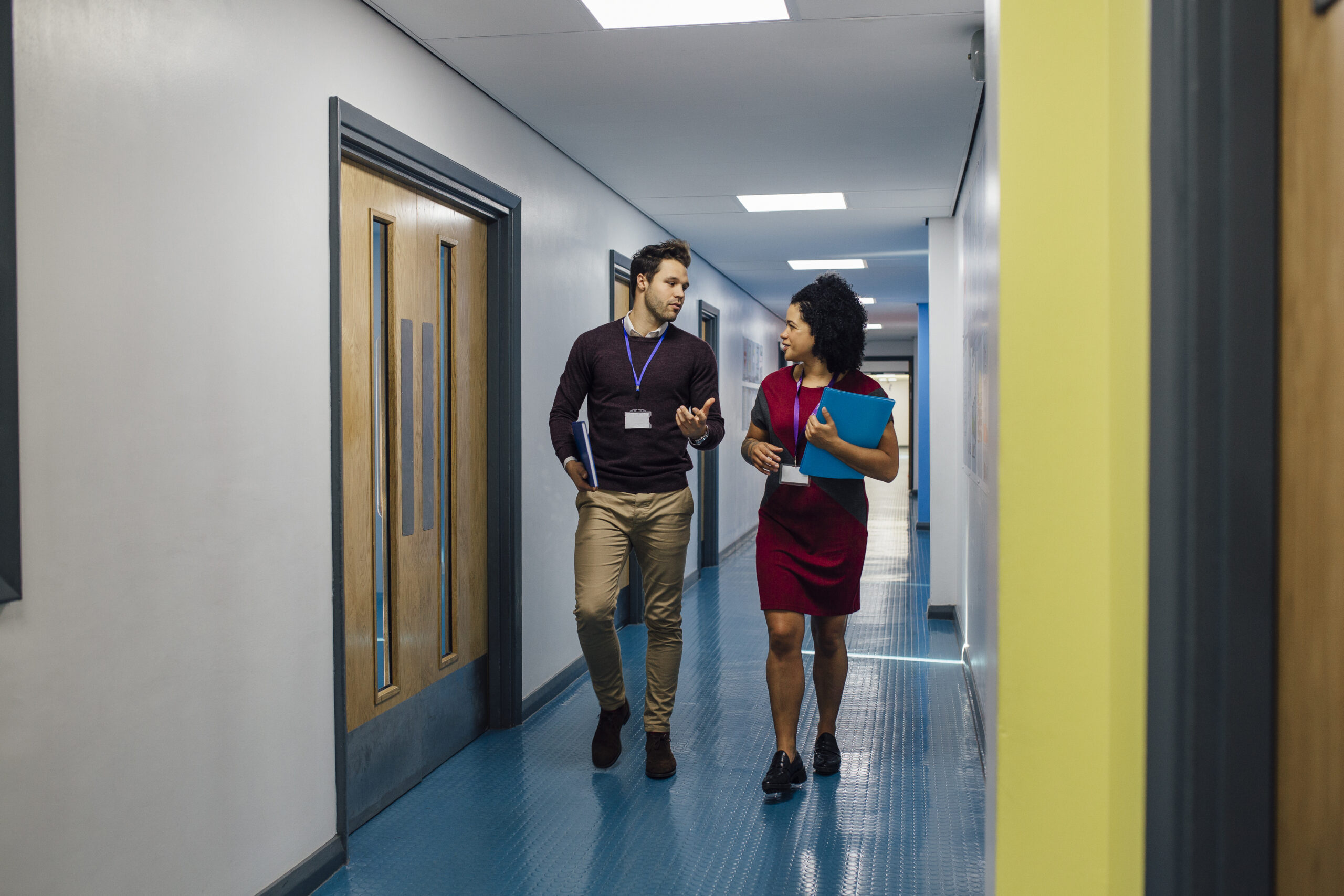 Two teachers are talking in the school hall as they walk to their next lesson together.