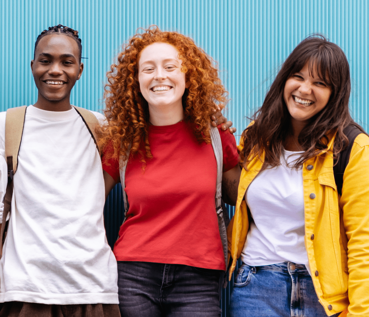 Three secondary students in bright colors, smiling, arms around each other.