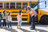 While waiting in line to board the school bus, an educator high-fives a young student.