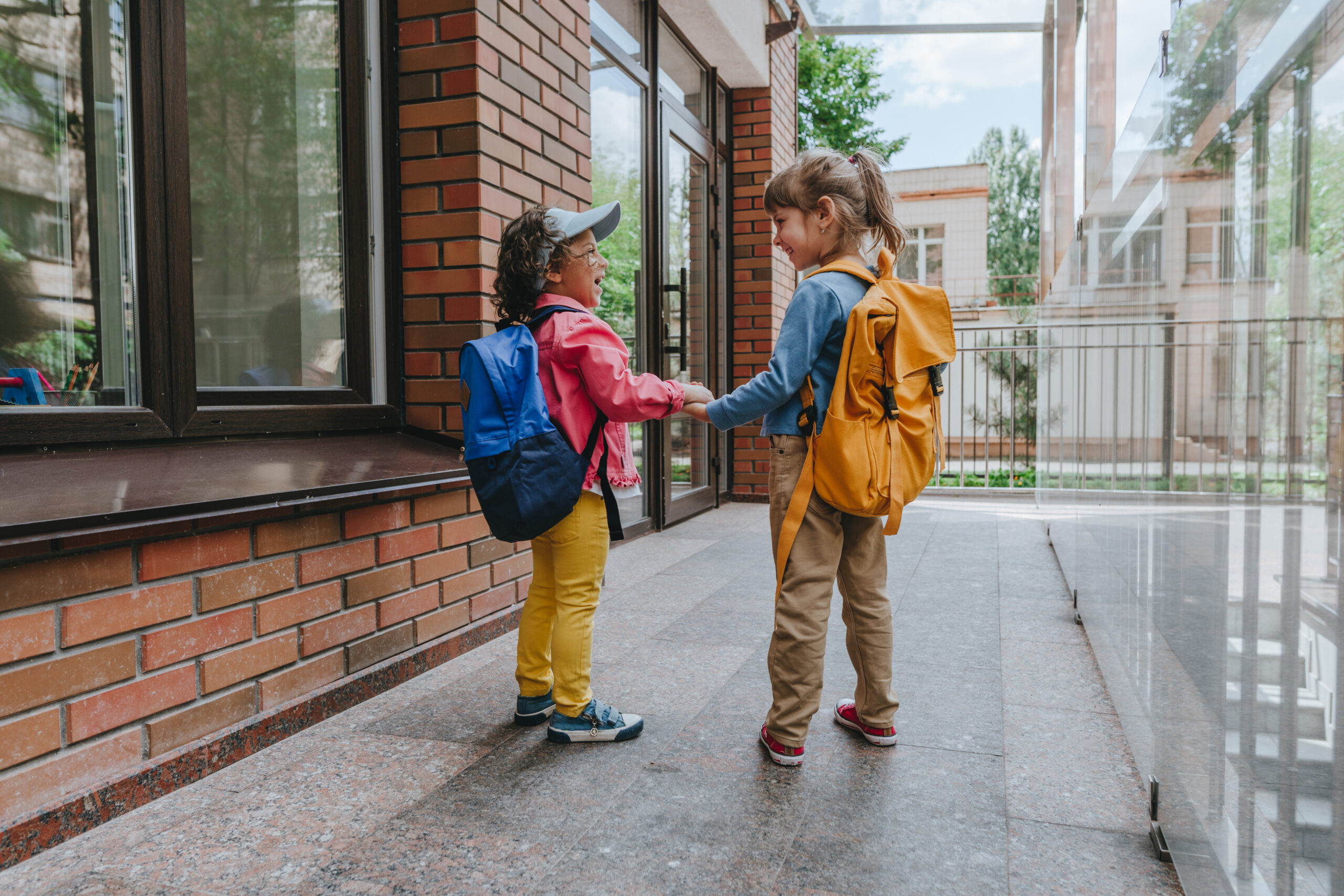 Two little girls with backpacks going to an elementary school.